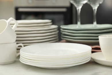 Photo of Clean plates and cups on white marble table in kitchen