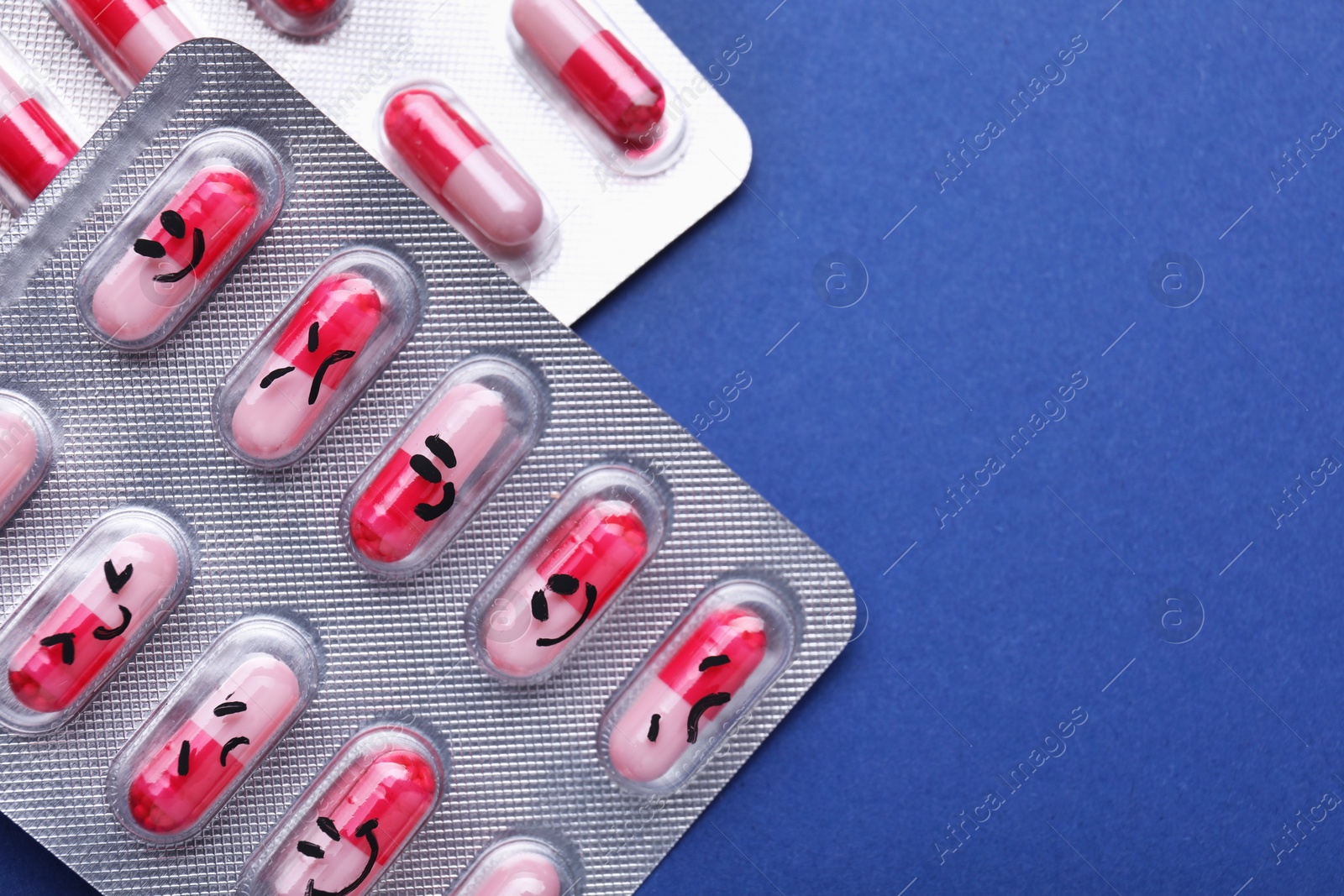 Photo of Blisters of antidepressant pills with emotional faces on blue background, flat lay. Space for text