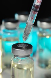 Filling syringe with medicine from vial against blurred background, closeup