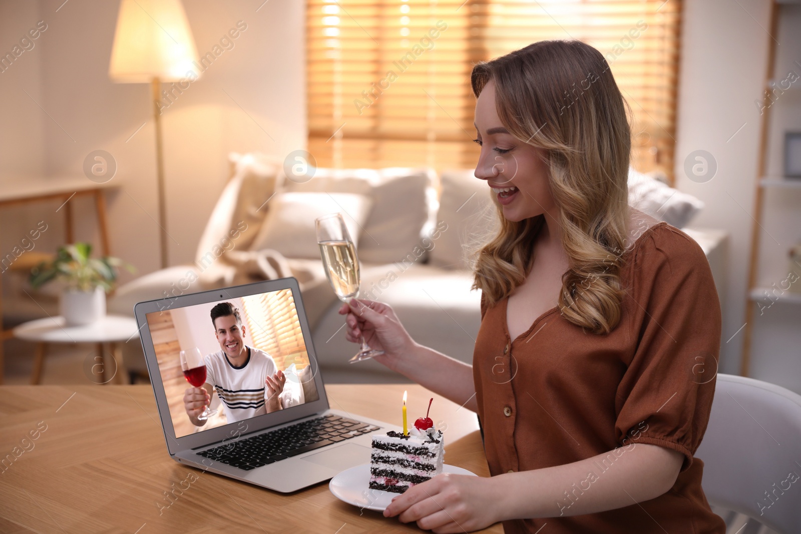 Image of Woman with glass of champagne and cake having online party via laptop at home during quarantine lockdown
