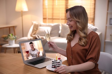 Woman with glass of champagne and cake having online party via laptop at home during quarantine lockdown