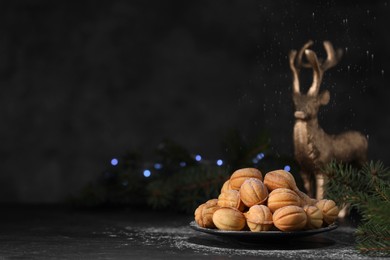 Plate of tasty nut shaped cookies near fir branches on black table. Space for text