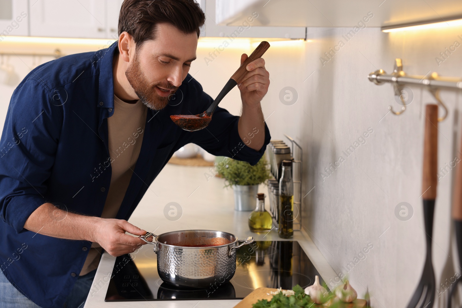 Photo of Man tasting delicious tomato soup in kitchen