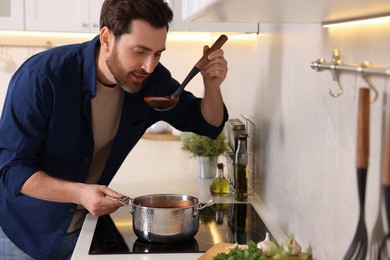 Photo of Man tasting delicious tomato soup in kitchen