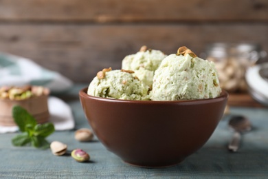 Photo of Delicious pistachio ice cream in bowl on blue wooden table