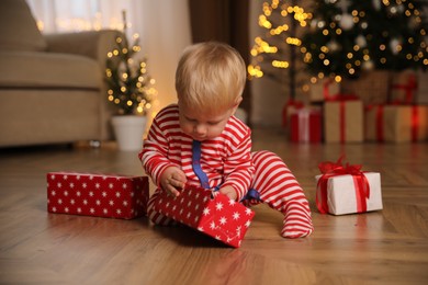 Photo of Baby in Christmas pajamas opening gift box indoors