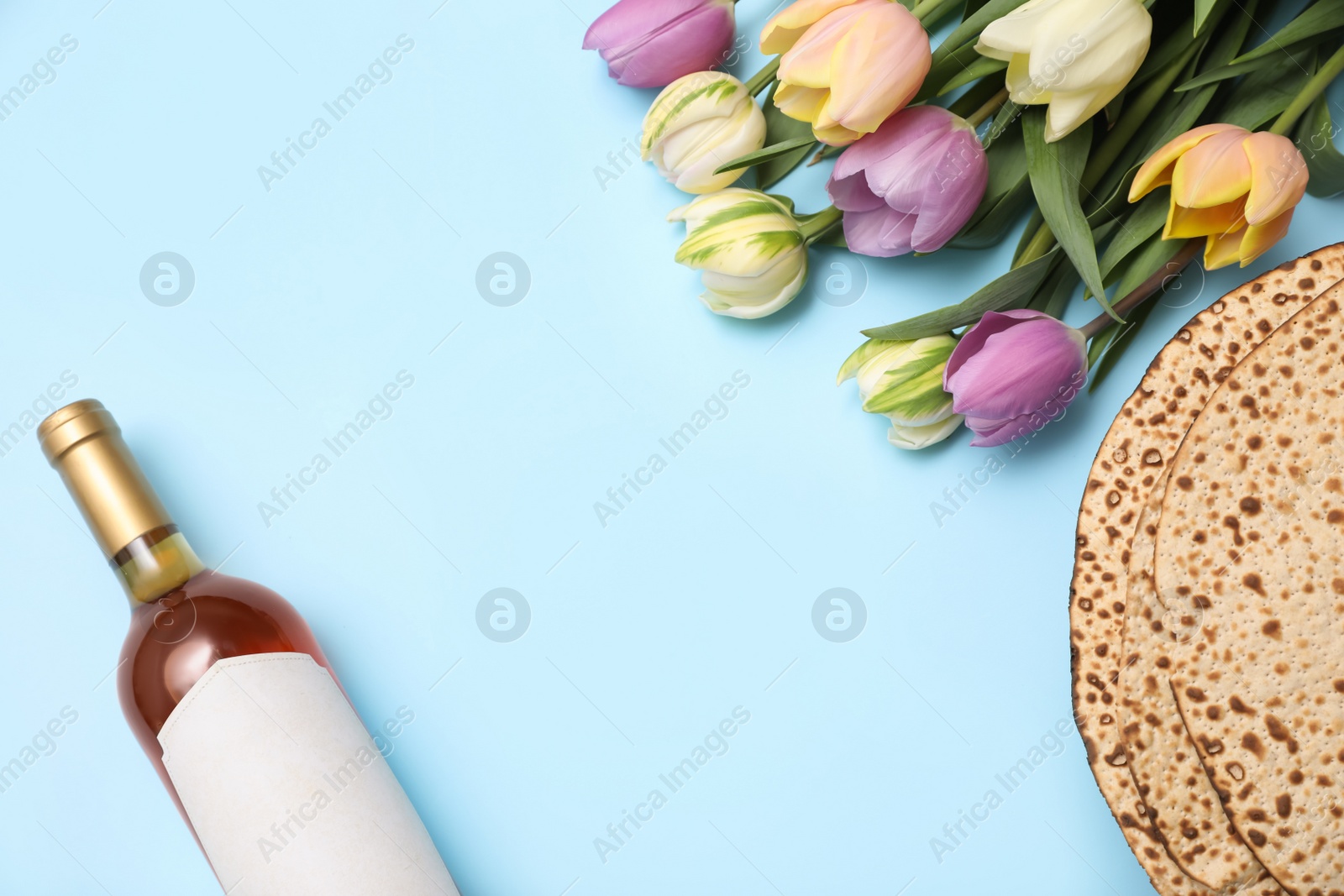 Photo of Tasty matzos, wine and tulips on light blue background, flat lay with space for text. Passover (Pesach) celebration