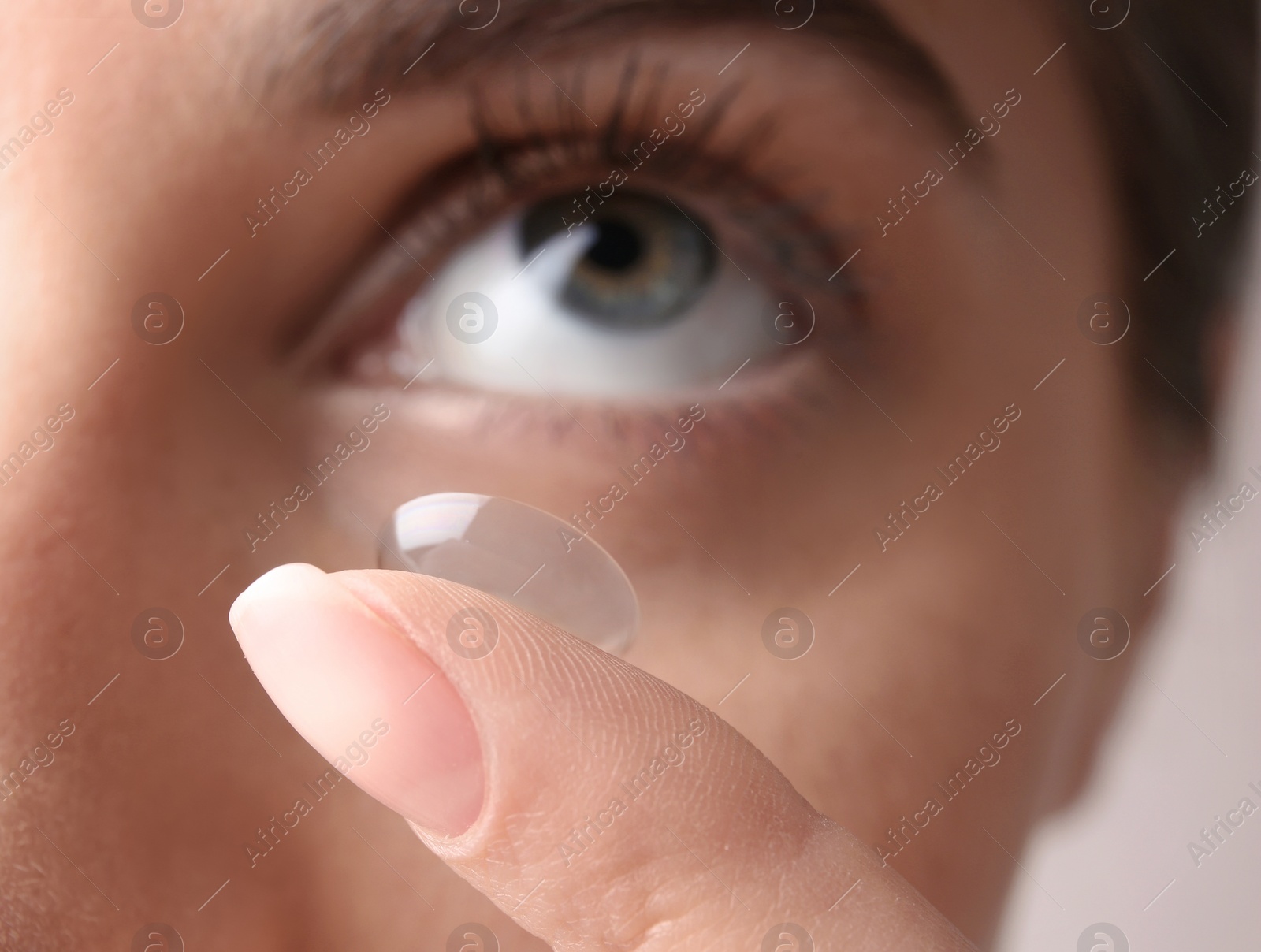 Photo of Young woman putting contact lens in her eye, closeup