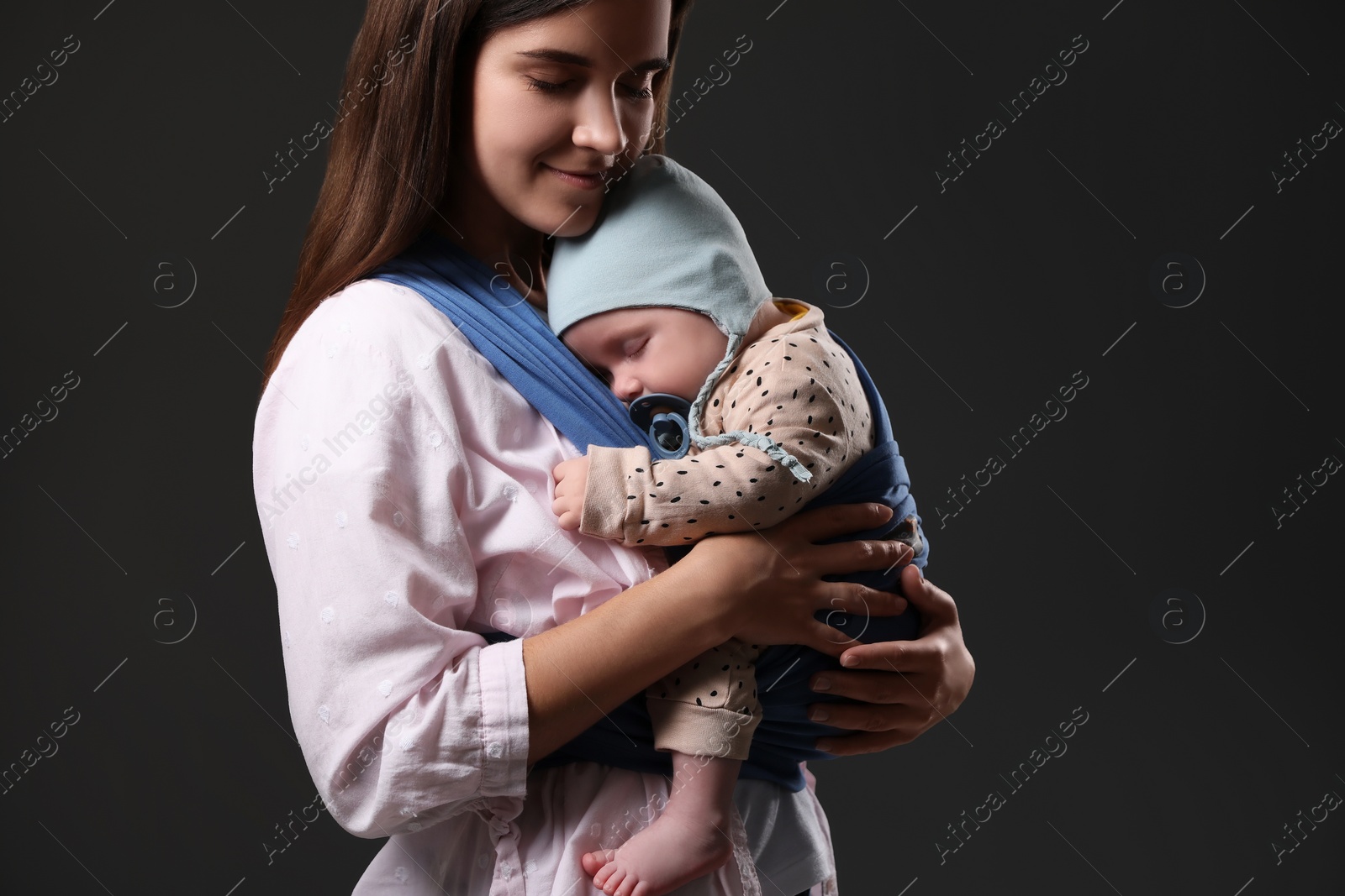 Photo of Mother holding her child in sling (baby carrier) on black background. Space for text