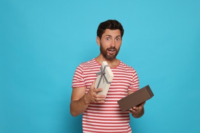 Photo of Emotional man opening gift box on turquoise background, space for text