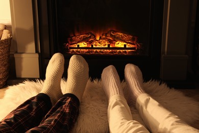 Photo of Couple in knitted socks near fireplace at home, closeup of legs