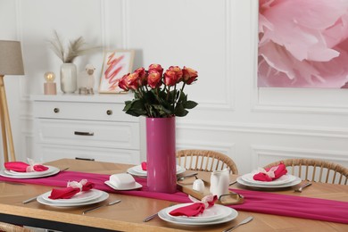 Color accent table setting. Plates, cutlery, pink napkins and vase with beautiful roses in dining room