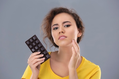 Photo of Beautiful young woman with acne problem holding chocolate on grey background. Skin allergy