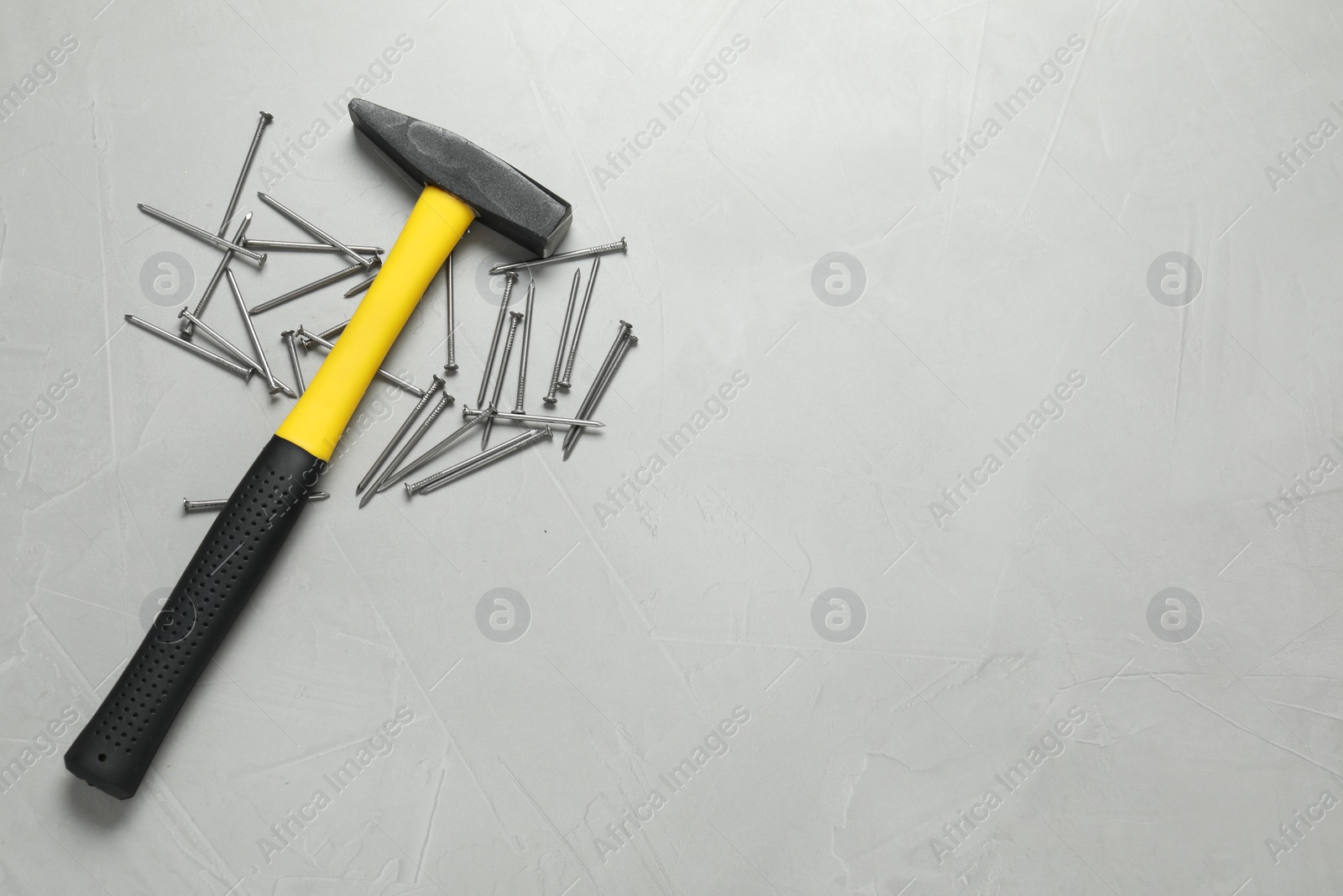 Photo of New hammer and metal nails on grey table, flat lay. Space for text