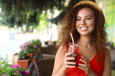 Happy African-American woman with glass of natural lemonade in cafe. Detox drink