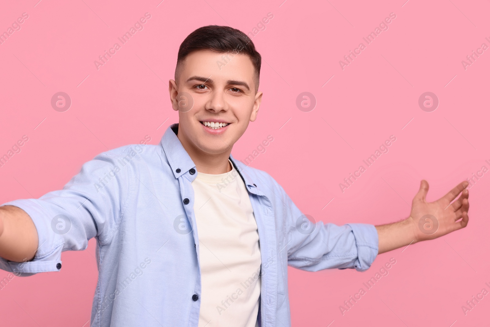 Photo of Handsome man inviting to come in against pink background