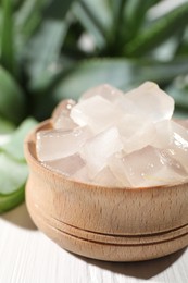 Photo of Aloe vera gel in bowl and slices of plant on white wooden table, closeup