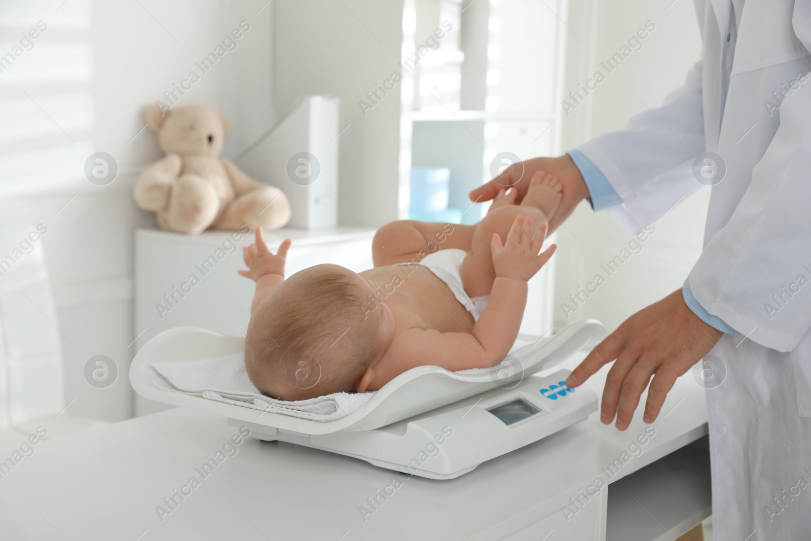 Photo of Pediatrician weighting cute baby in clinic, closeup. Health care