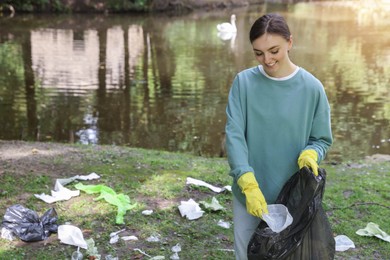 Photo of Young woman with plastic bag collecting garbage in park