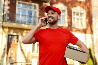 Courier with parcel talking on smartphone outdoors. Order delivery