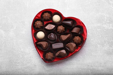 Heart shaped box with delicious chocolate candies on light grey table, top view