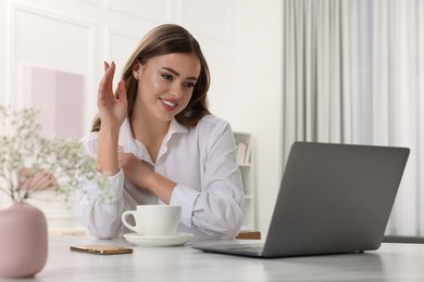 Photo of Happy woman having video chat via laptop at white table in room
