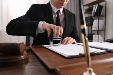 Photo of Notary stamping document at wooden table in office, closeup