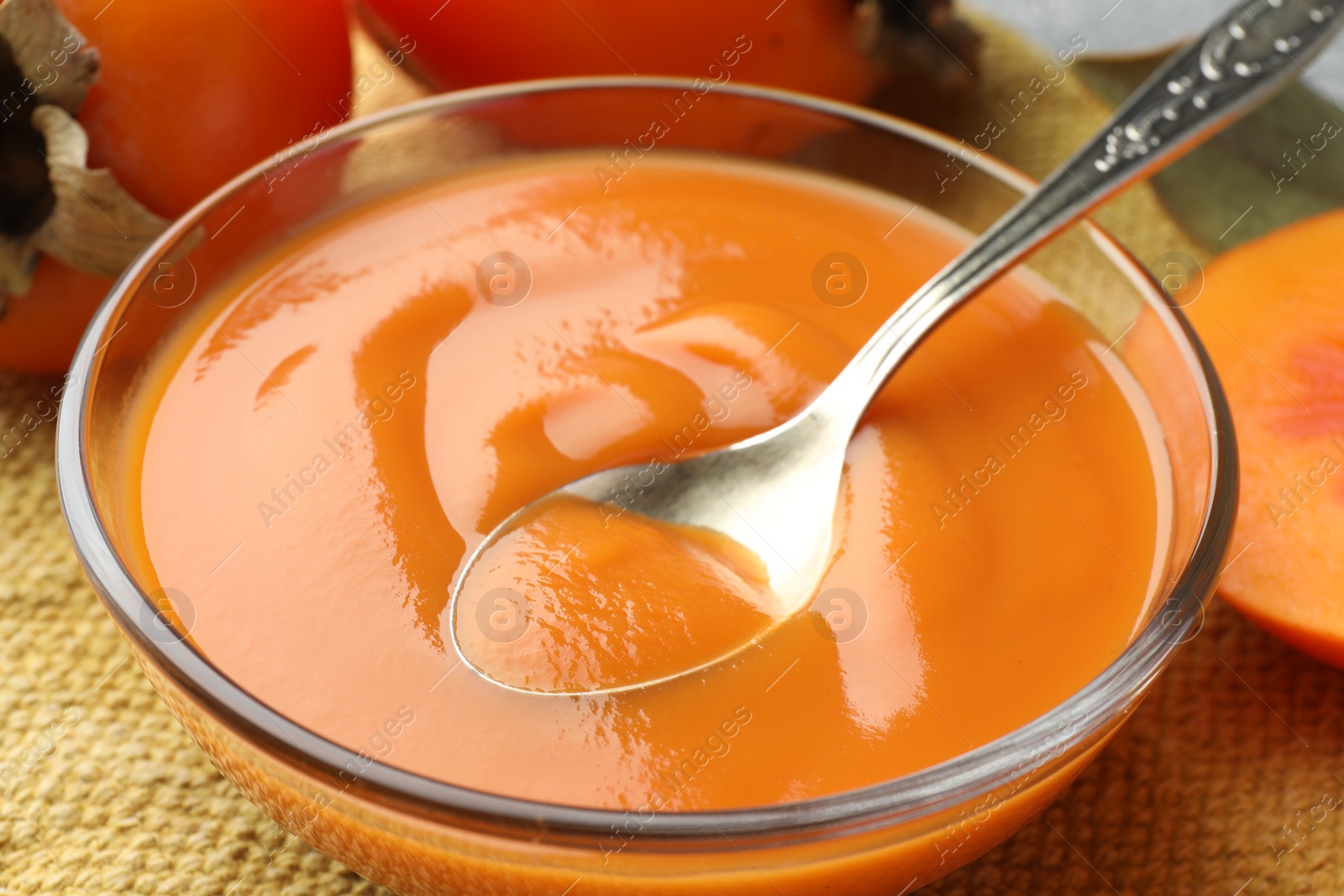 Photo of Taking delicious persimmon jam with spoon from bowl on table, closeup