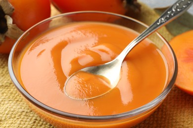 Taking delicious persimmon jam with spoon from bowl on table, closeup