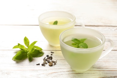 Photo of Cups with hot aromatic mint tea, fresh and dry leaves on wooden table
