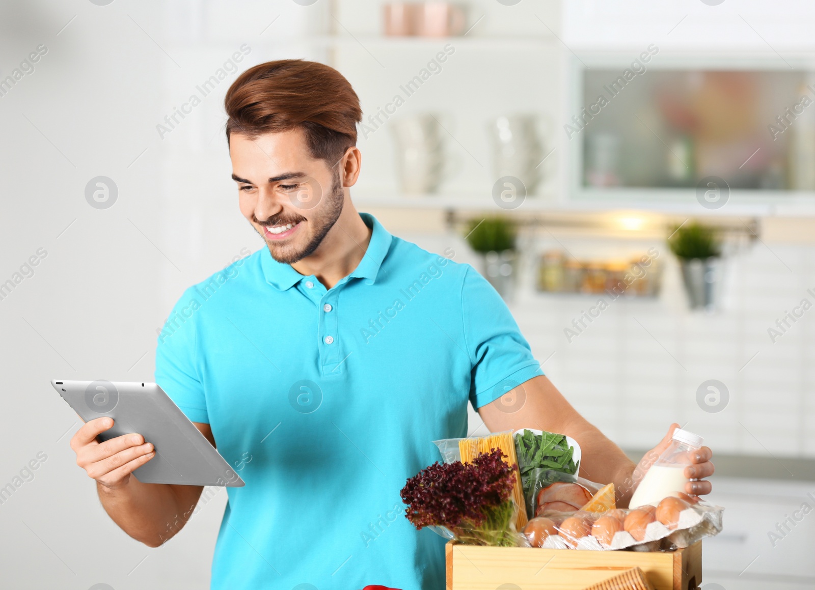 Photo of Young man with tablet PC and products in kitchen. Food delivery service