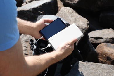 Man charging mobile phone with power bank on rocky mountain, closeup