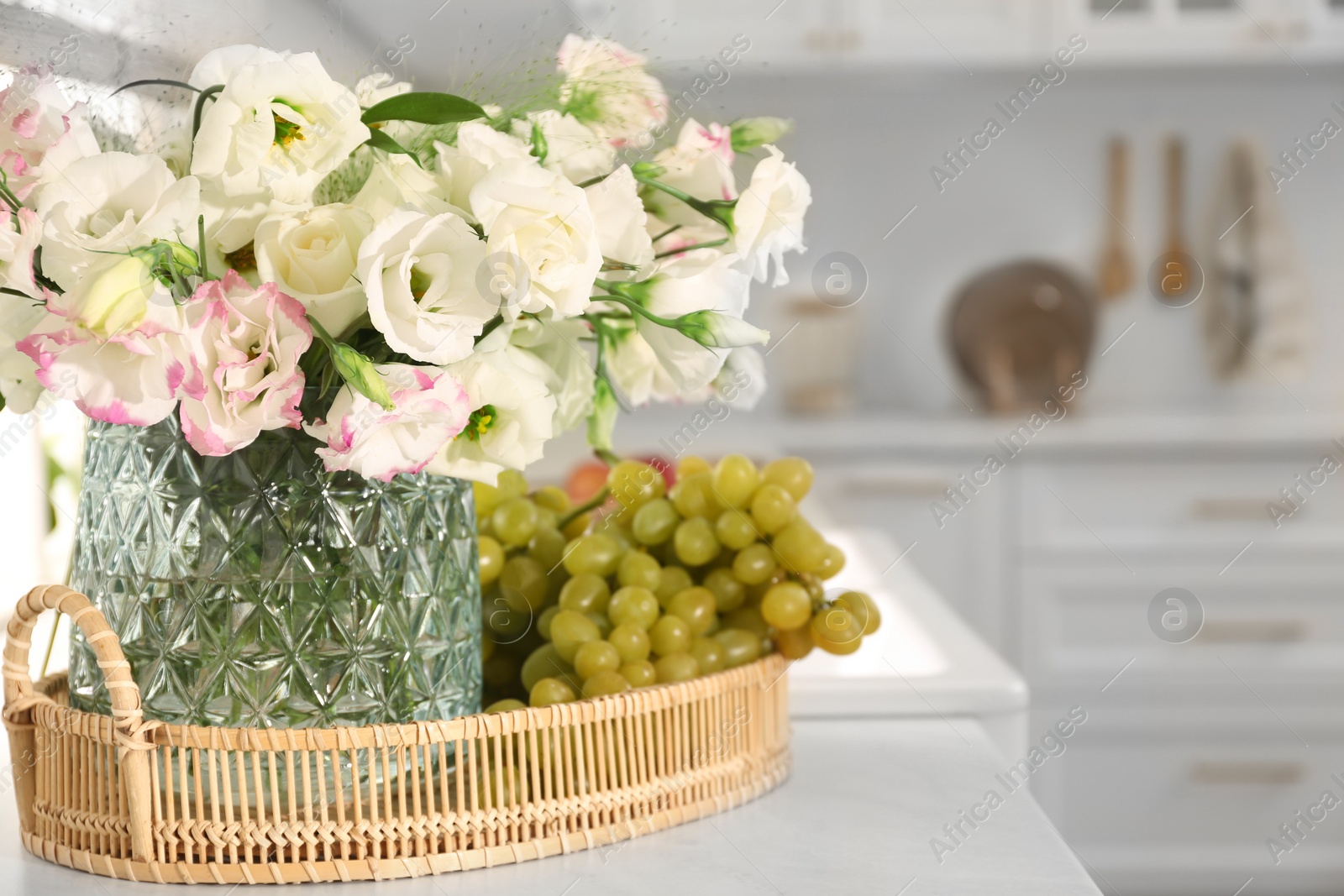 Photo of Bouquet of beautiful eustoma flowers and grapes on white table in kitchen. Interior design