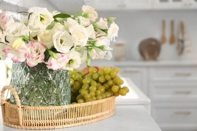 Photo of Bouquet of beautiful eustoma flowers and grapes on white table in kitchen. Interior design