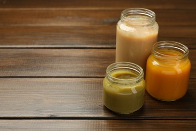 Photo of Tasty baby food in jars on wooden table. Space for text