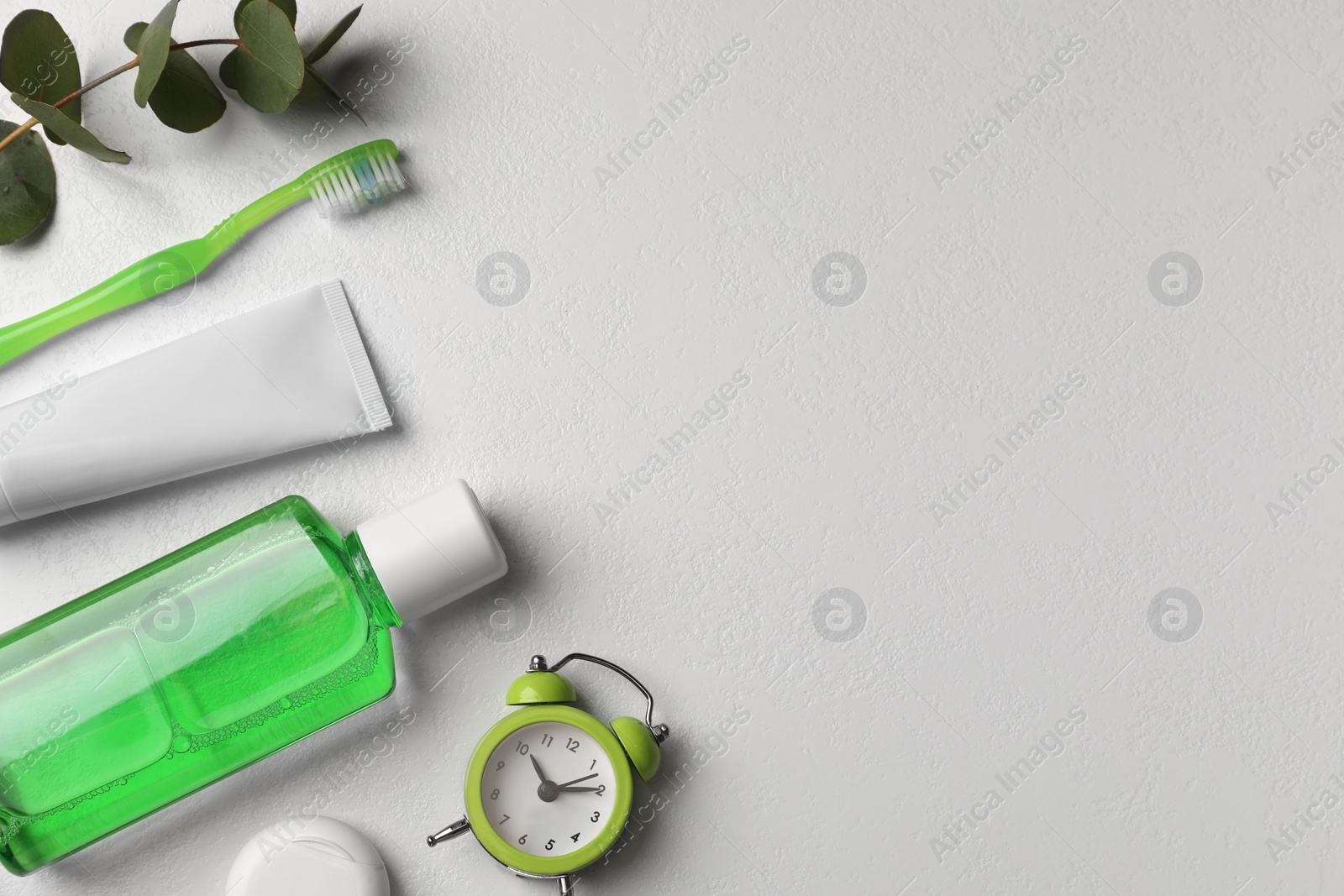 Photo of Fresh mouthwash in bottle, toothbrush, toothpaste, dental floss and alarm clock on light background, flat lay. Space for text