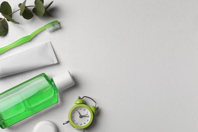 Fresh mouthwash in bottle, toothbrush, toothpaste, dental floss and alarm clock on light background, flat lay. Space for text