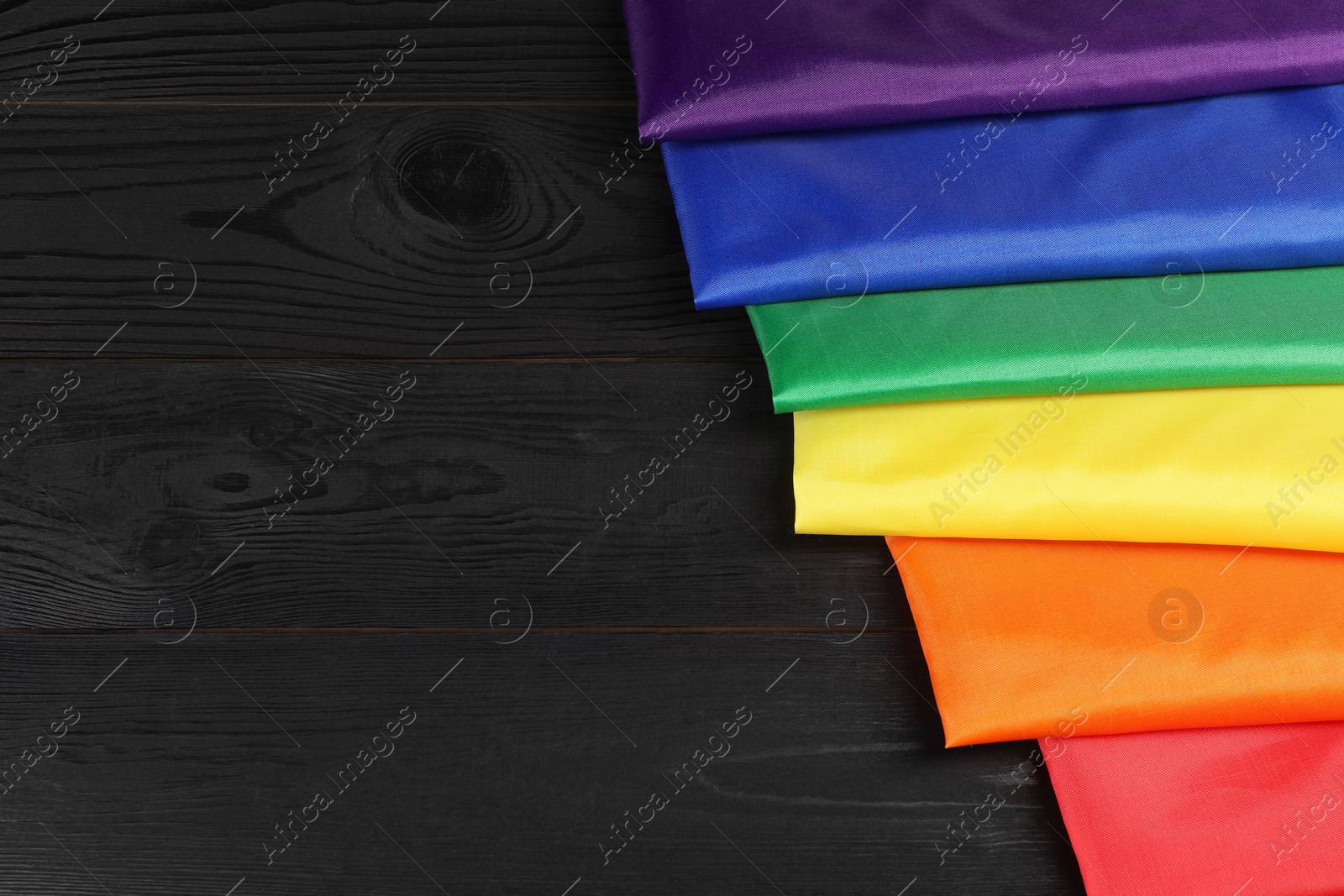 Photo of Rainbow LGBT flag on black wooden background, closeup. Space for text