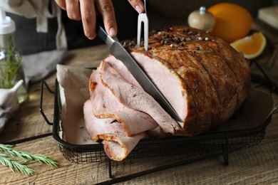 Woman cutting delicious baked ham at wooden table, closeup