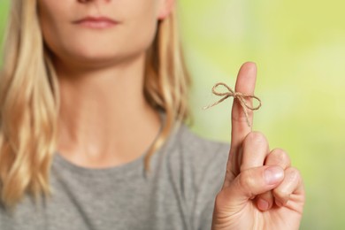 Photo of Woman showing index finger with tied bow as reminder against green blurred background, focus on hand
