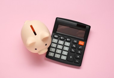 Photo of Calculator and piggy bank on pink background, top view