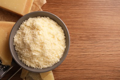Photo of Delicious grated parmesan cheese in bowl on wooden table, flat lay. Space for text