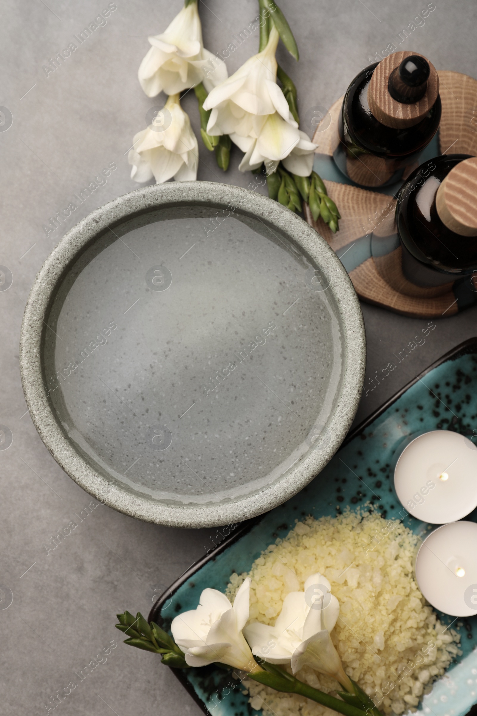 Photo of Flat lay composition with essential oil, sea salt and beautiful flowers on grey table. Aromatherapy treatment