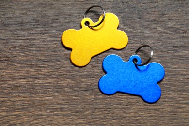 Photo of Color metal pet tags in shape of bones with ring on wooden table, flat lay. Space for text