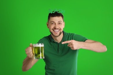 Image of Happy man in St. Patrick's Day outfit with beer on green background