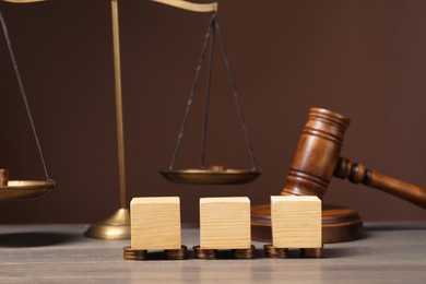 Law. Blank cubes, coins and gavel on wooden table against brown background