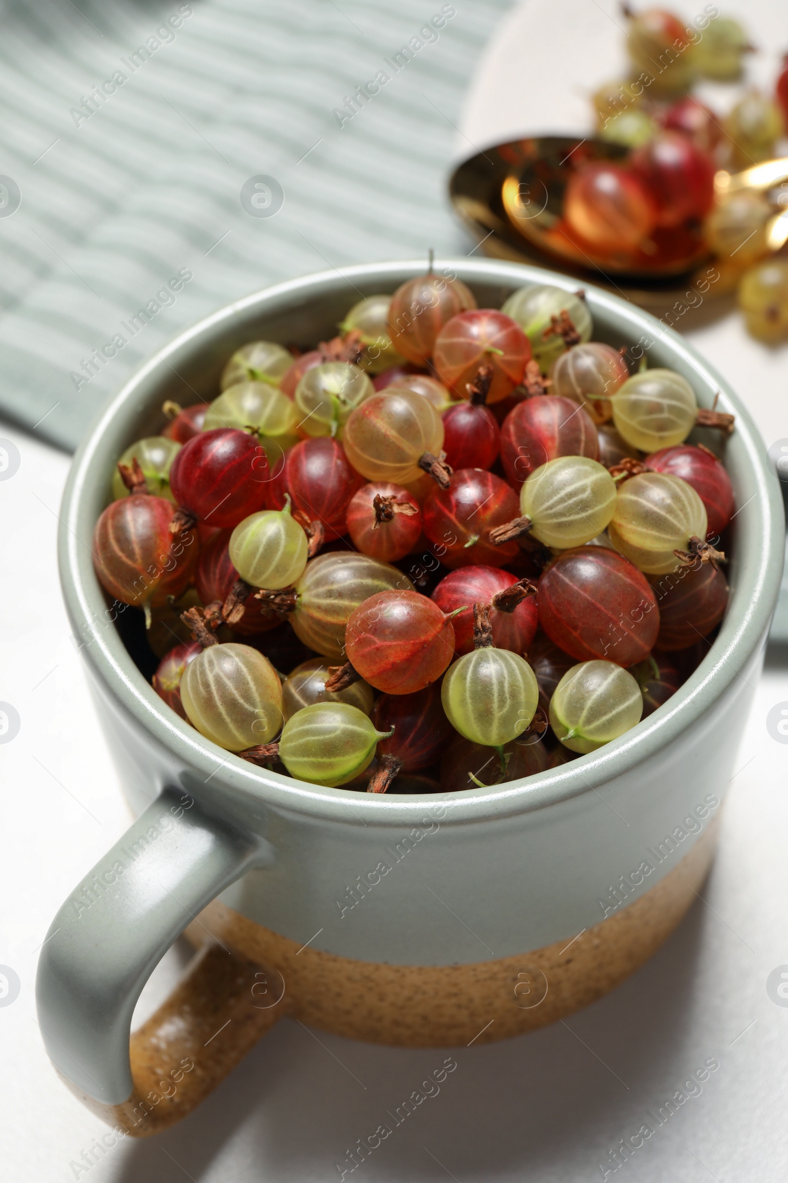 Photo of Cup with fresh ripe gooseberries on white table, closeup