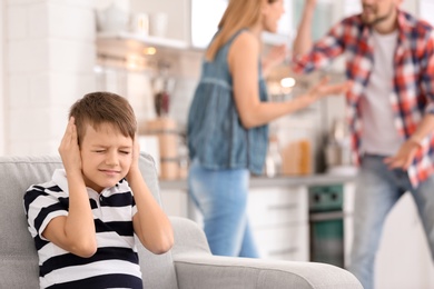 Photo of Little unhappy boy sitting on sofa while parents arguing at home