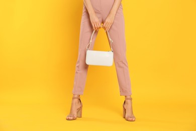 Woman with stylish bag on yellow background, closeup