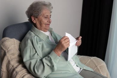 Photo of Elderly woman with letter in armchair indoors. Loneliness concept